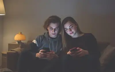 Dva lidé sedí blízko sebe na pohovce, každý u svého telefonu